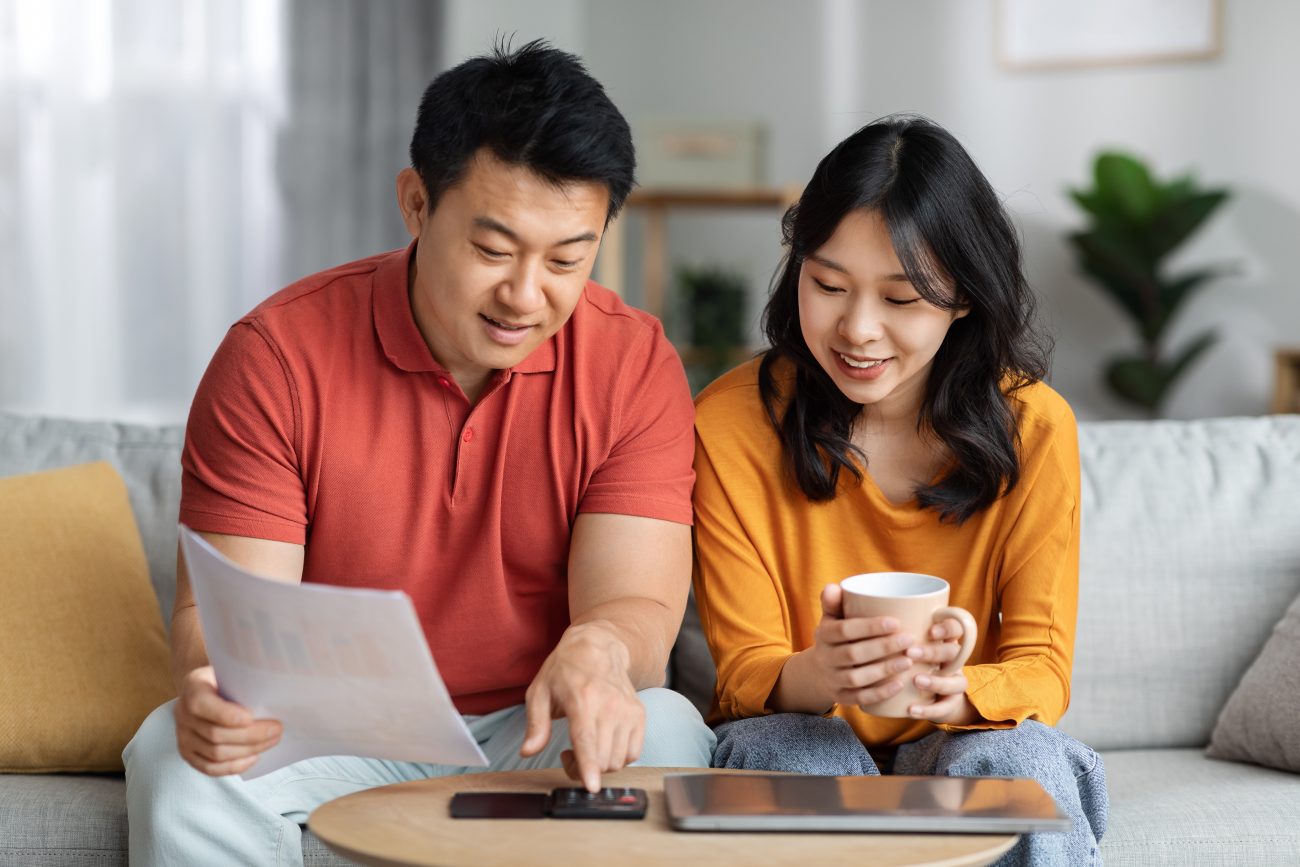 Asian man and woman sitting at table looking at family budget.